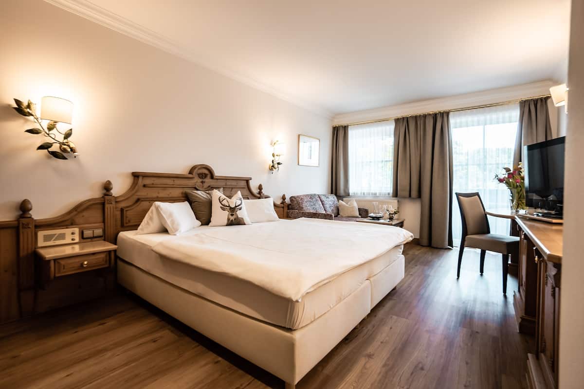 Une chambre d’hôtel avec un grand lit, un bureau avec une chaise, une télévision et une fenêtre avec des rideaux.