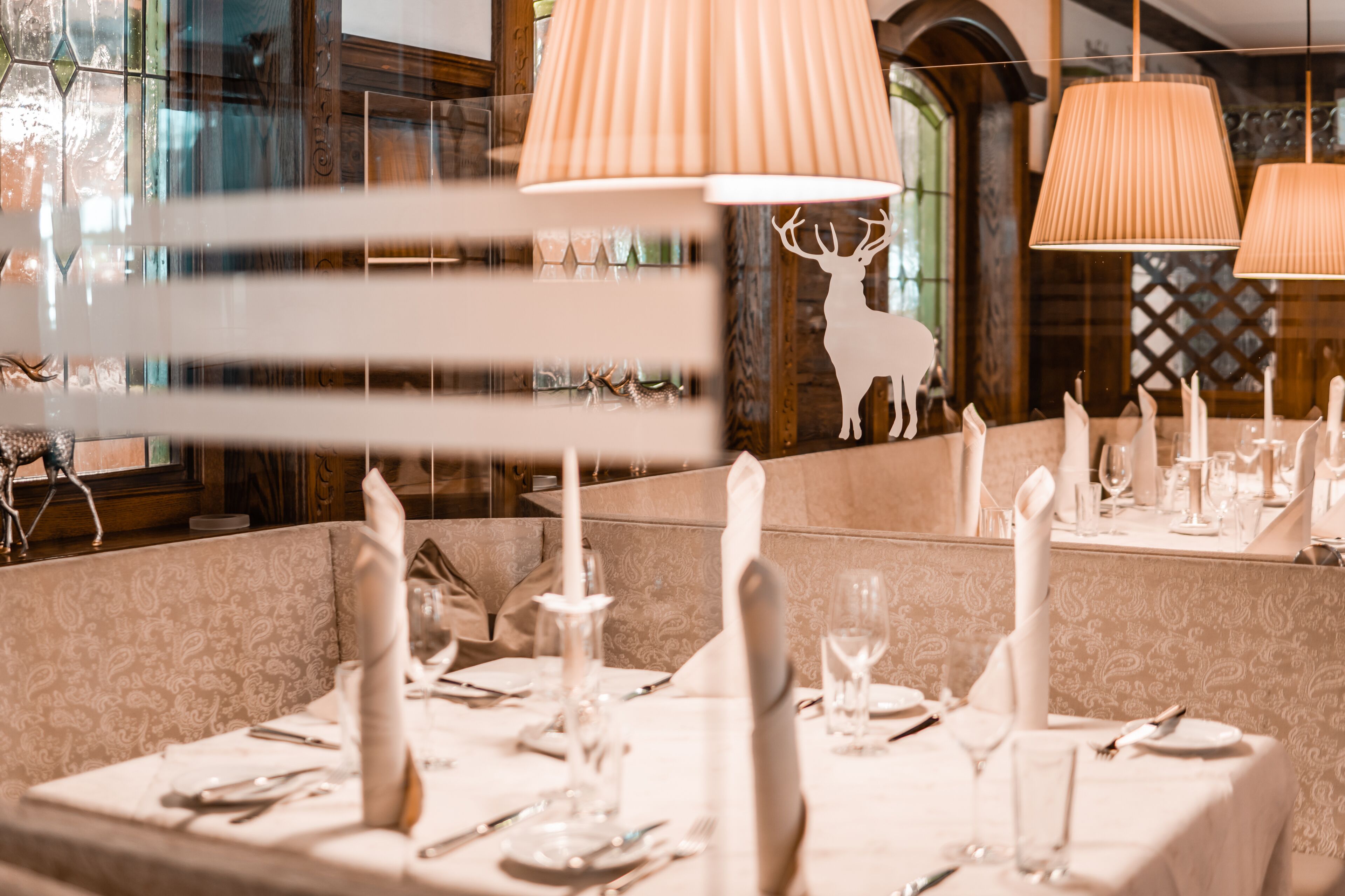A dining area with tables set for a meal, featuring white tablecloths, candles, and a deer silhouette on the wall.