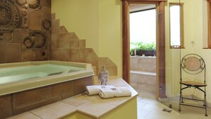 Un baño con una bañera grande, un revestimiento decorativo, una pequeña estatua de Buda y un letrero que dice "CALIDIUM".