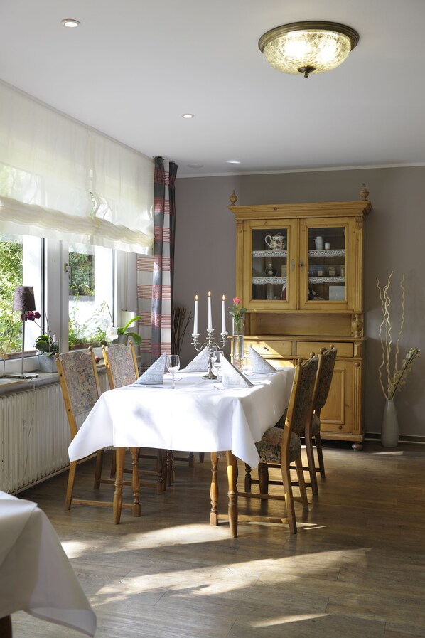 A dining room with a table set for four, wooden chairs, a cabinet with glass doors, and a window with curtains.