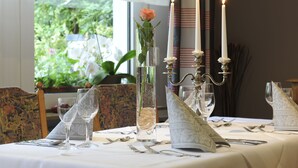 Mesa lista para cenar con velas, un florero con una flor y vistas al exterior con vegetación.