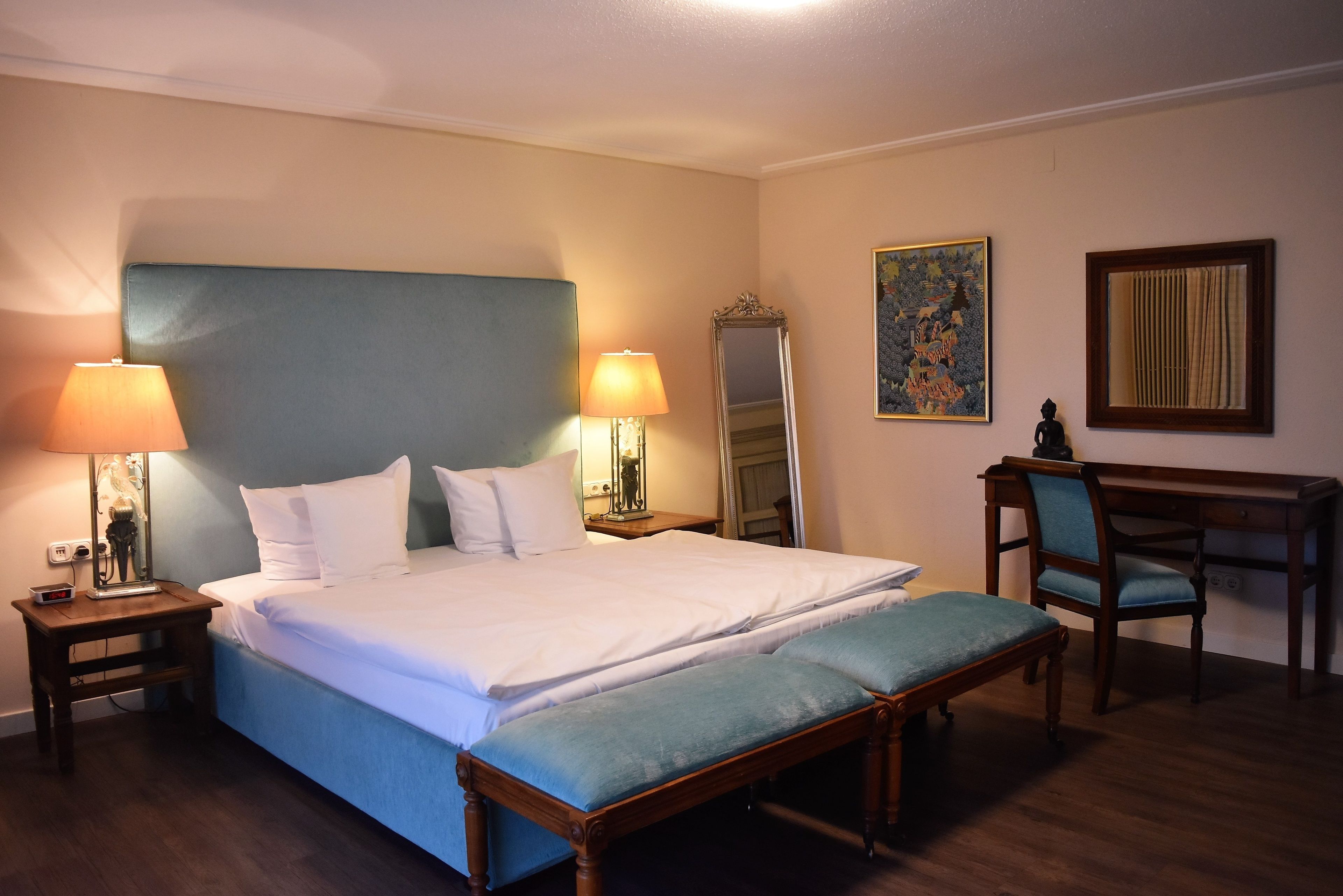 Une chambre d’hôtel avec un grand lit, deux lampes de chevet, un bureau avec une chaise et un miroir.
