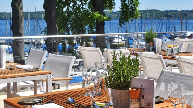 Un espace extérieur aménagé pour les repas, avec des tables et des chaises, donnant sur une marina où sont amarrés des bateaux.