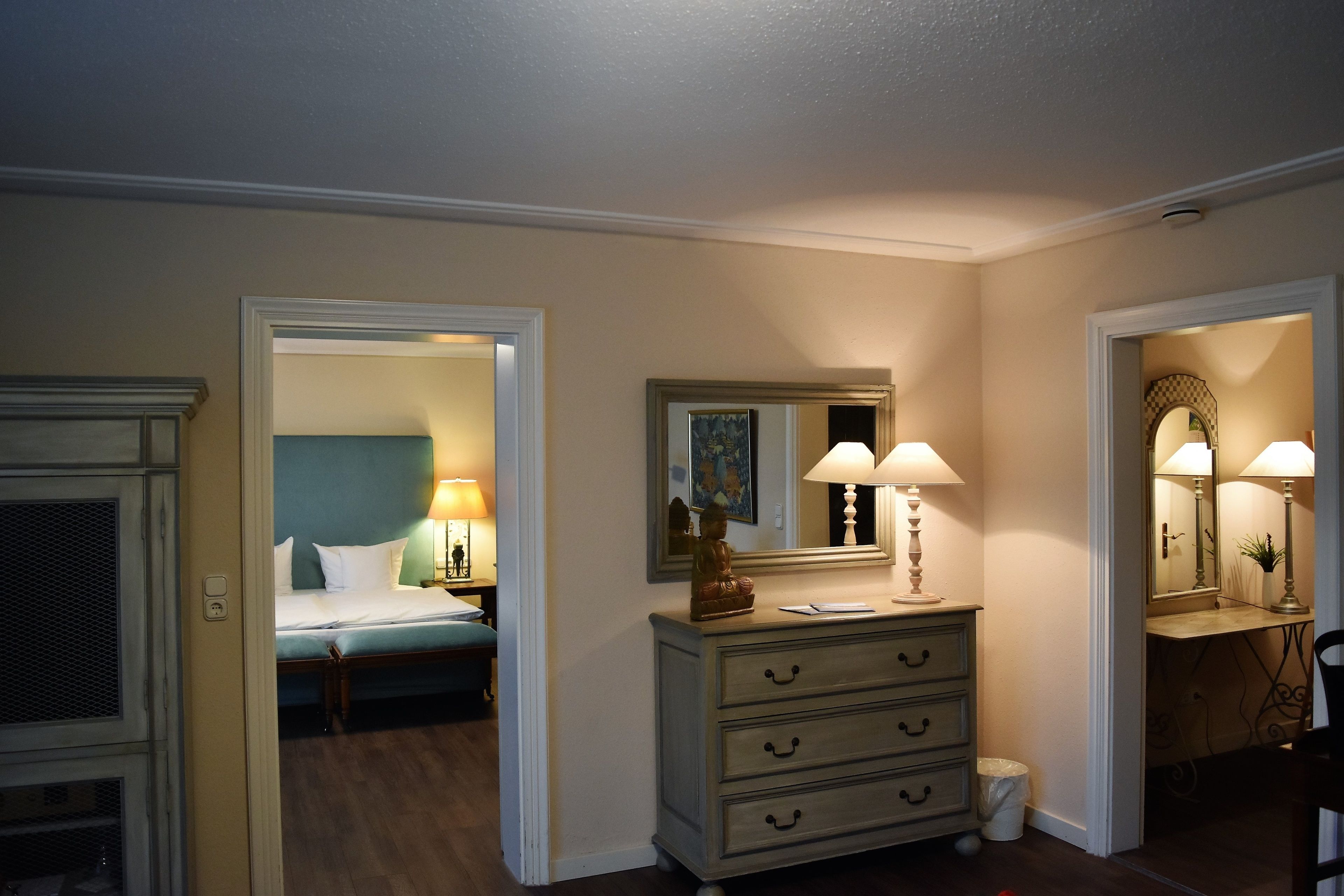 Habitación de hotel con cama, cómoda y dos espejos. Se ve una puerta que da a otra habitación.