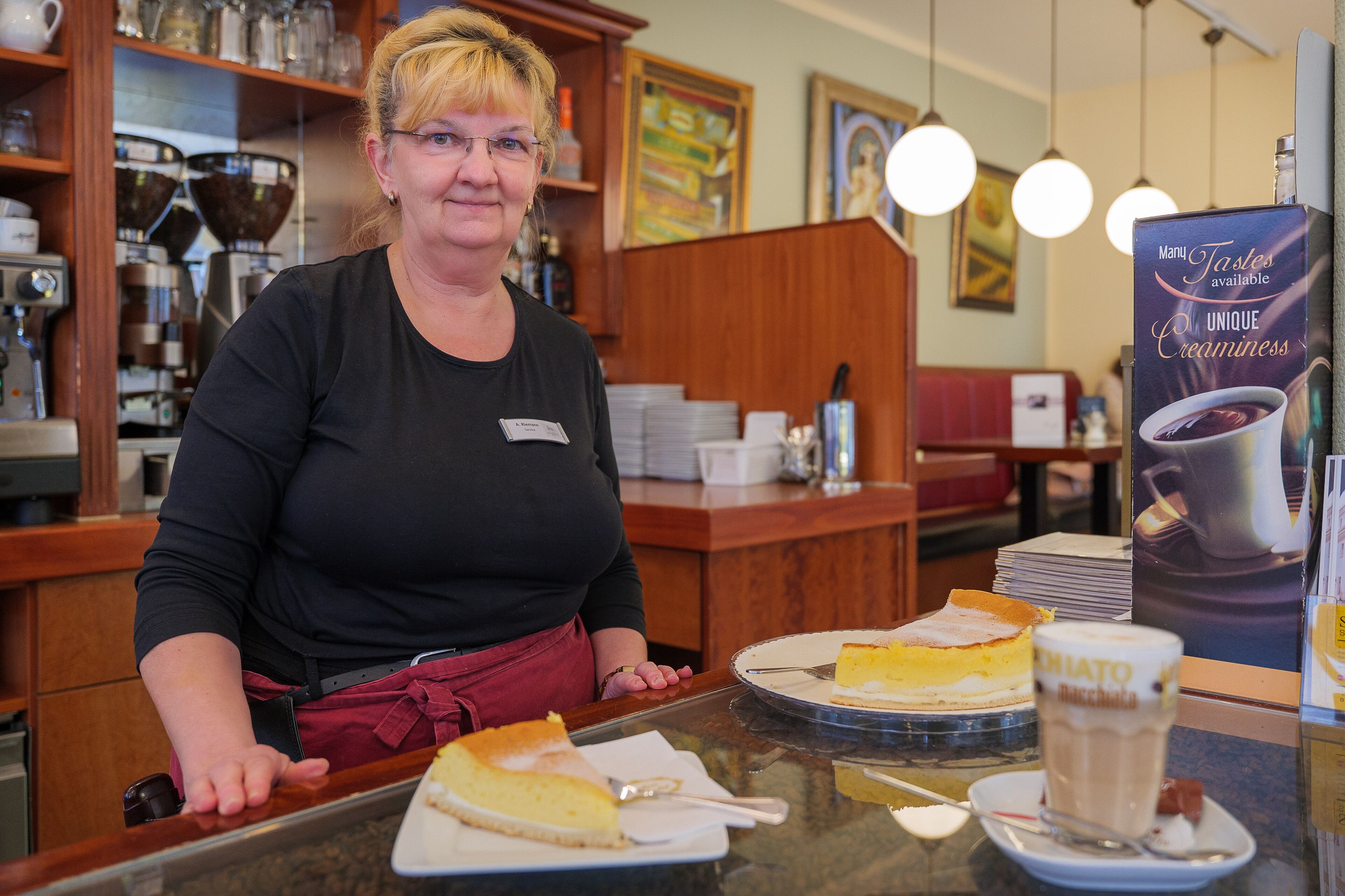 Une personne se tient derrière un comptoir, et un panneau affiche une sélection de desserts.