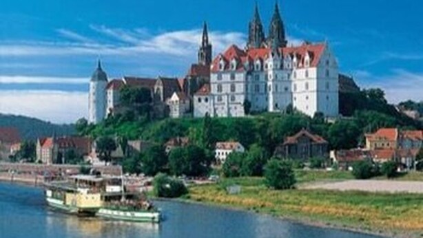 A large castle with multiple towers, situated on a hill overlooking a river.