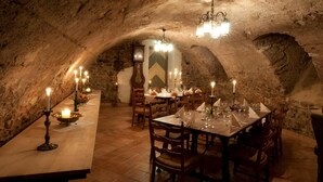 A dining area with a long table set for multiple people, surrounded by stone walls and a chandelier.