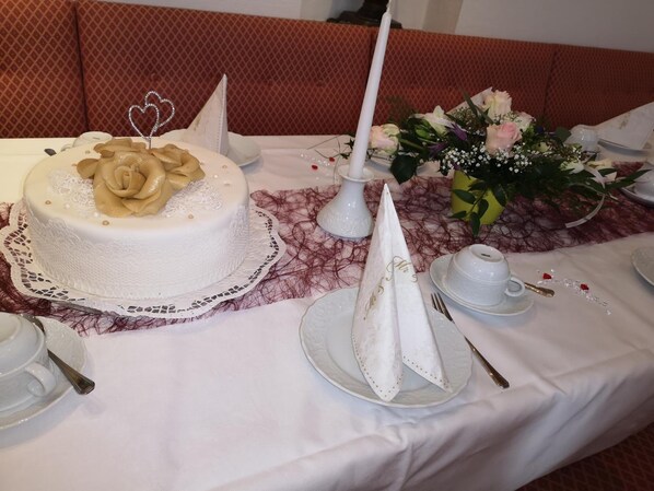 Una mesa decorada con un pastel blanco, una vela blanca, un ramo de flores y vajilla blanca.