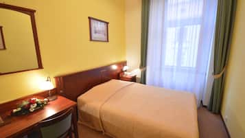 Een hotelkamer met een bed, een bureau met lamp, een stoel, een nachtkastje met lamp, een lijst met afbeelding aan de muur en een raam met gordijnen.