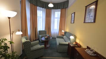 Een kamer met een bank, twee fauteuils, een kleine tafel met een vaas en een lamp.