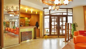 A hotel lobby with a reception desk, orange seating, a large window, and a modern chandelier. - Grandhotel Garni (Jihlava)
