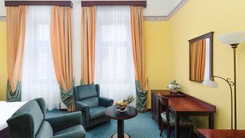 A hotel room with a bed, two armchairs, a small table with fruit, a desk, and a lamp.