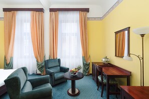 A hotel room with a bed, two armchairs, a small table with fruit, a desk, and a lamp. - Grandhotel Havel (Jihlava)