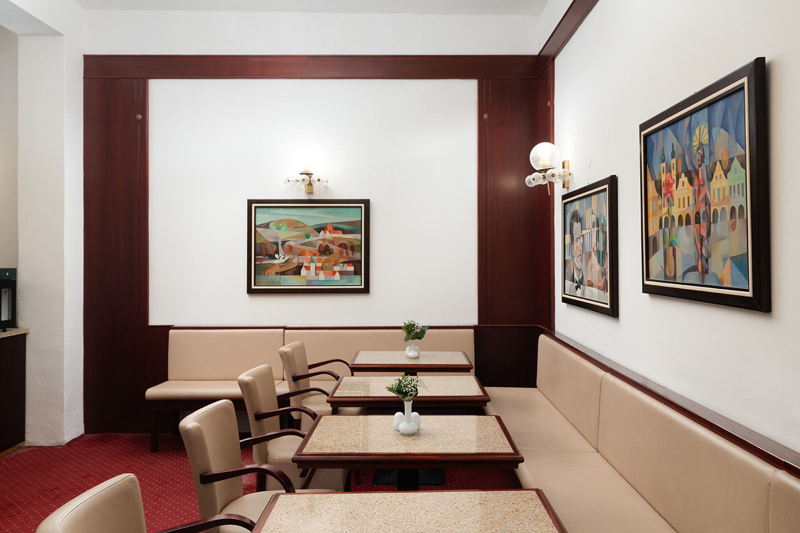Un espace de restauration d’hôtel avec des banquettes et des tables, des œuvres d’art aux murs et un tapis rouge.