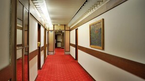 A hotel hallway with a red carpet, wooden paneling, and a painting on the wall. - Grandhotel Garni (Jihlava)