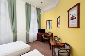 Una habitación de hotel con una cama, un escritorio con televisor, una mesa de comedor con sillas y un frutero.