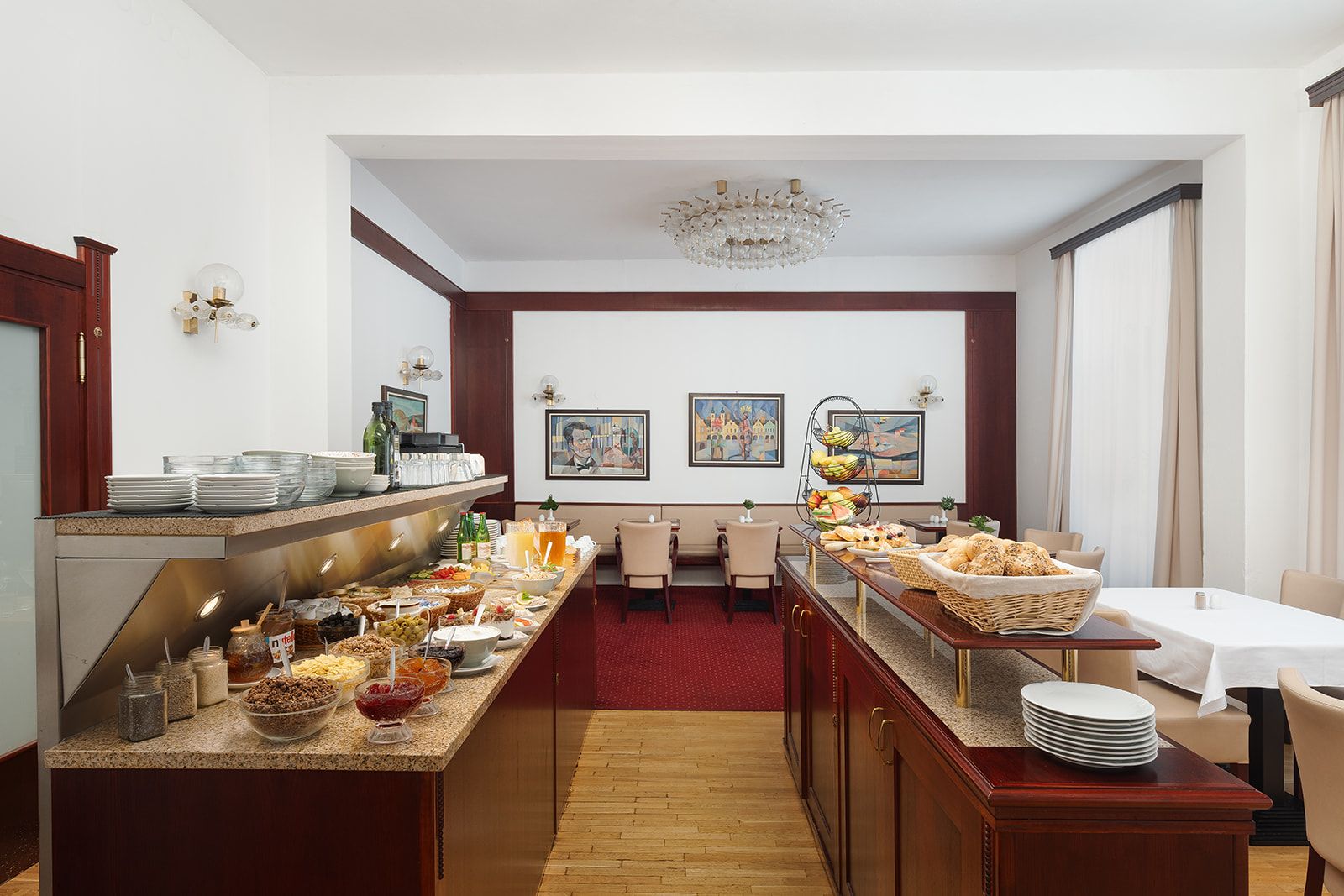 Een hotelontbijtbuffet met diverse gerechten, een zithoek met tafels en stoelen, en kunstwerken aan de muur.