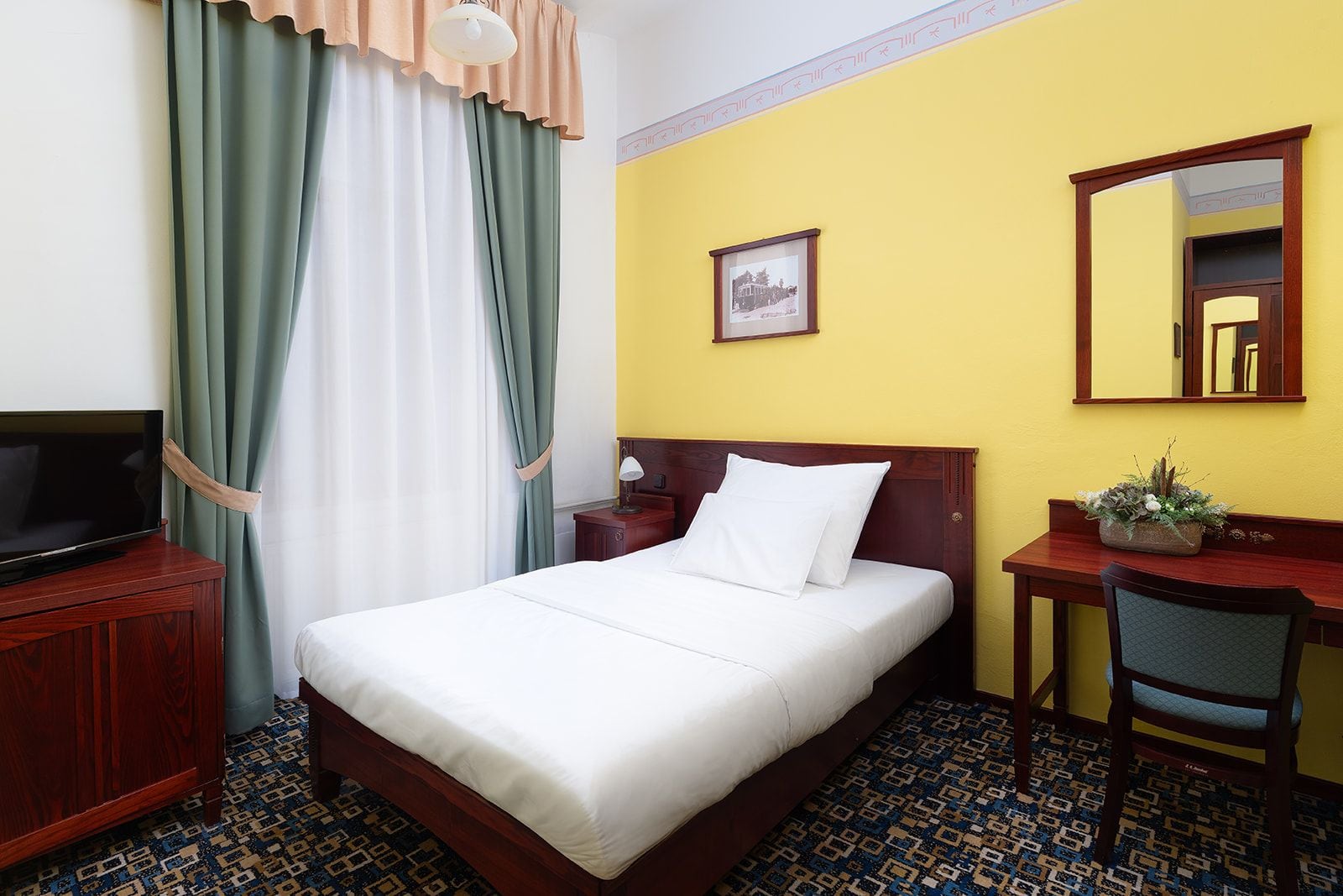 A hotel room with a bed, a desk, a chair, a television, and a mirror.