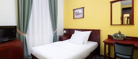 Habitación de hotel con cama, escritorio, silla, televisor y espejo.