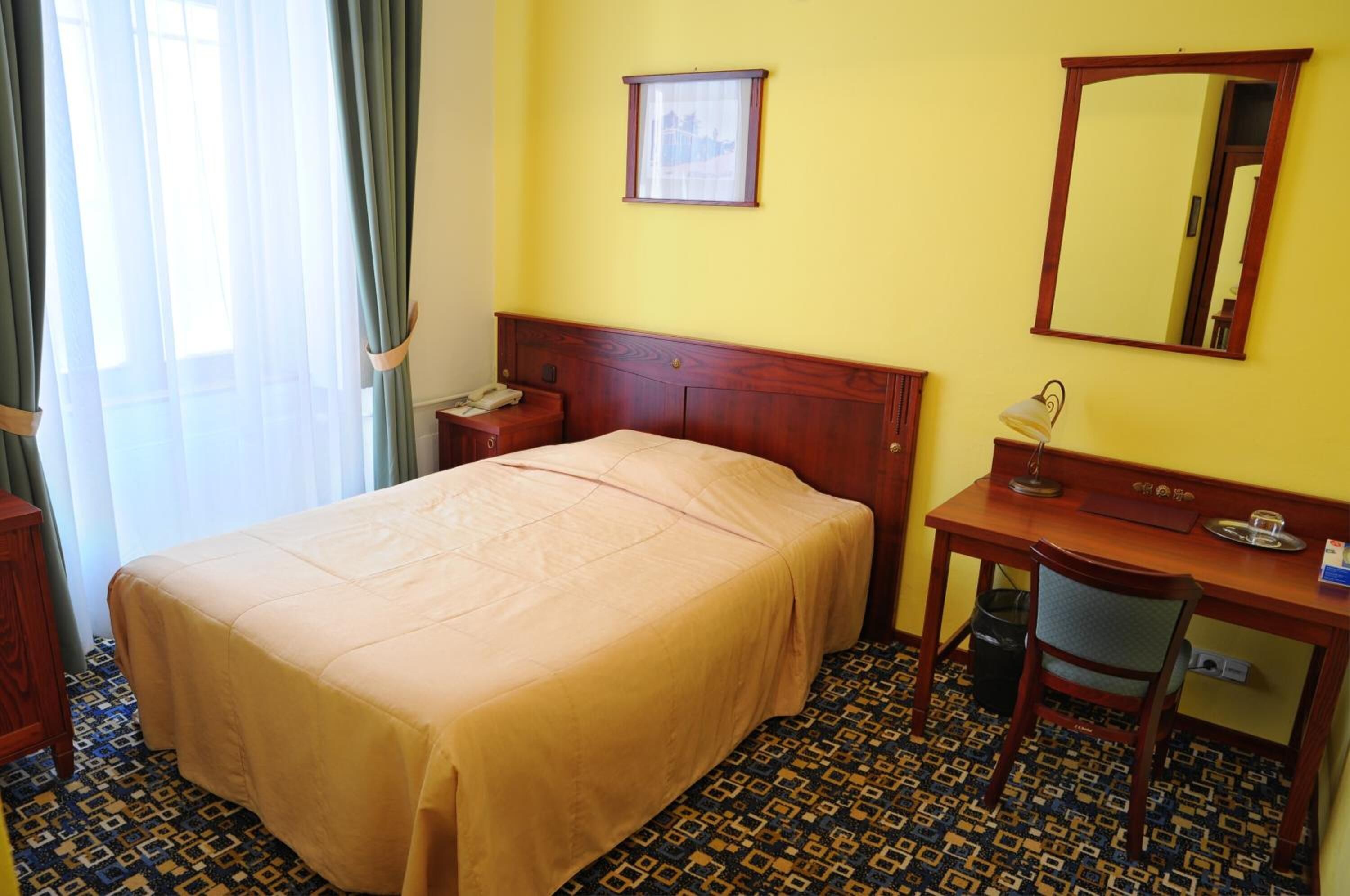 Ein Hotelzimmer mit Bett, Schreibtisch, Stuhl, Telefon, Spiegel und einem Fenster mit Vorhängen.