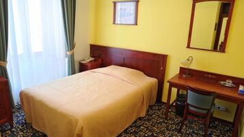 Ein Hotelzimmer mit Bett, Schreibtisch, Stuhl, Telefon, Spiegel und einem Fenster mit Vorhängen.