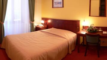Habitación de hotel con cama, escritorio, silla, televisor, lámpara y espejo.