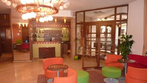 A lobby with orange and green seating, a bar area, and a large chandelier. - Grandhotel Garni (Jihlava)