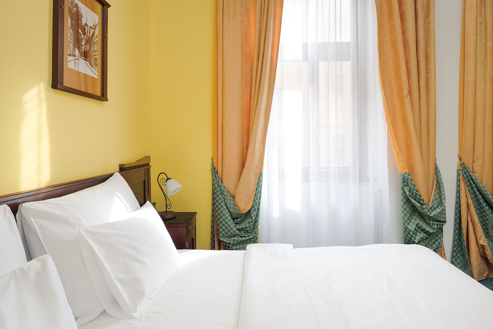 Une chambre d’hôtel avec un lit, une table de chevet, une lampe et des rideaux.