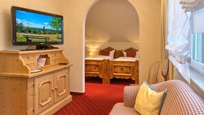 A cozy room with a wooden desk, a television, a bed with a red polka dot carpet, and a checkered sofa.