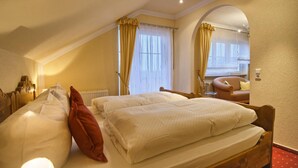 A hotel room with two beds, a sitting area with a chair and a table, and a large window with curtains.
