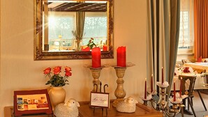 A dining area with a wooden table, red candles, a mirror, and a framed menu.