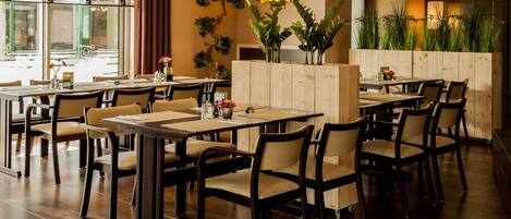 A restaurant interior with wooden tables and chairs, a neon sign, and potted plants.