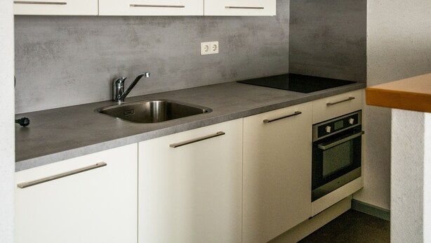 A kitchen with a stainless steel sink, a built-in oven, and white cabinets. - Dekkers Hotel (Ossendrecht)