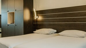 A hotel room with a bed, two pillows, a wooden headboard, and a wardrobe with a shelf. - Dekkers Hotel (Ossendrecht)