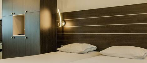 Una habitación de hotel con una cama, dos almohadas, un cabecero de madera y un armario con un estante.