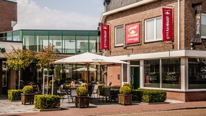A restaurant with outdoor seating, a brick facade, and multiple banners advertising the establishment. - Dekkers Hotel (Ossendrecht)