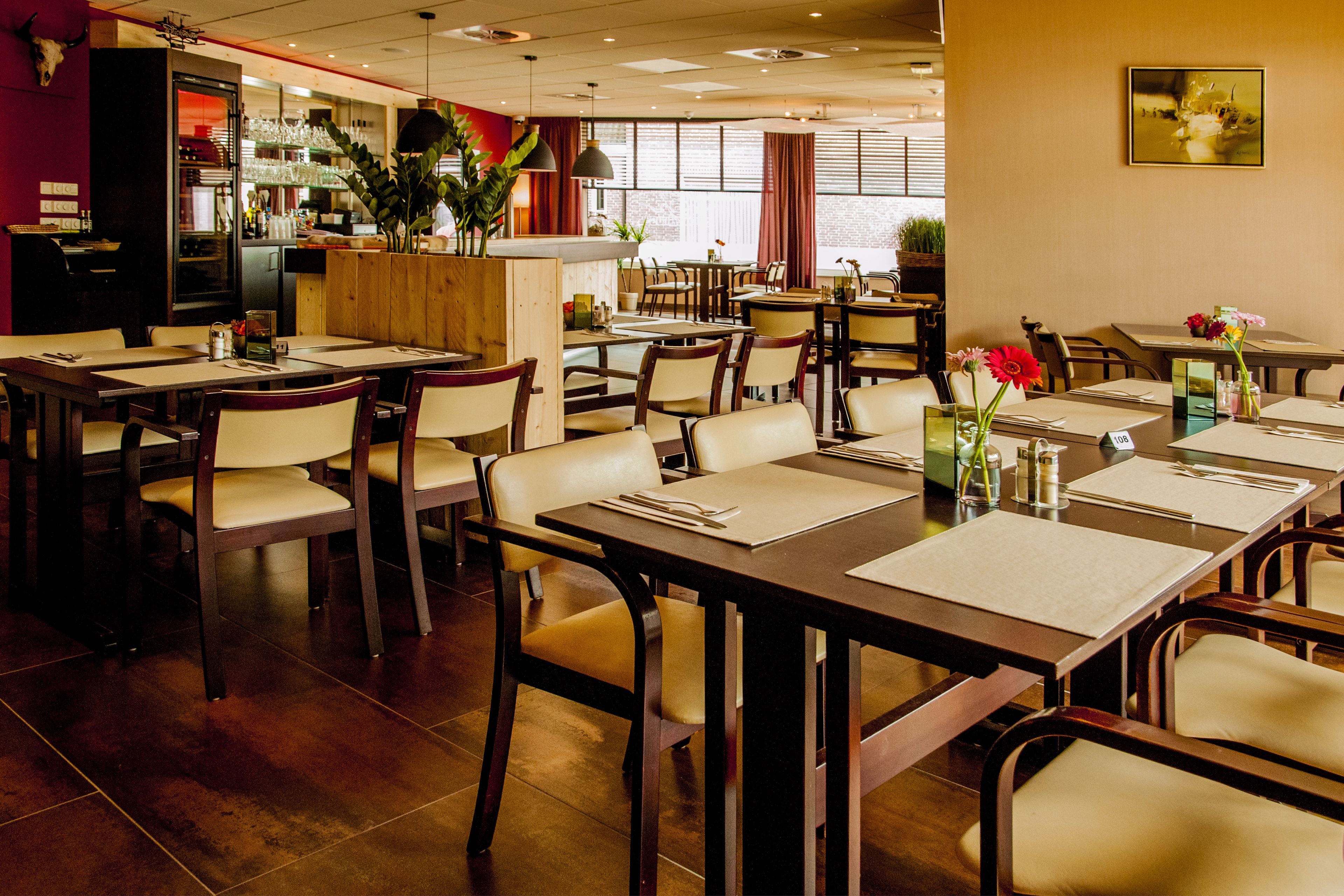 Un restaurant avec des tables et des chaises en bois, un coin bar et de grandes fenêtres.
