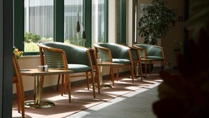 A seating area with four chairs and a table, large windows with sheer curtains, and a potted plant. - Dekkers Hotel (Ossendrecht)