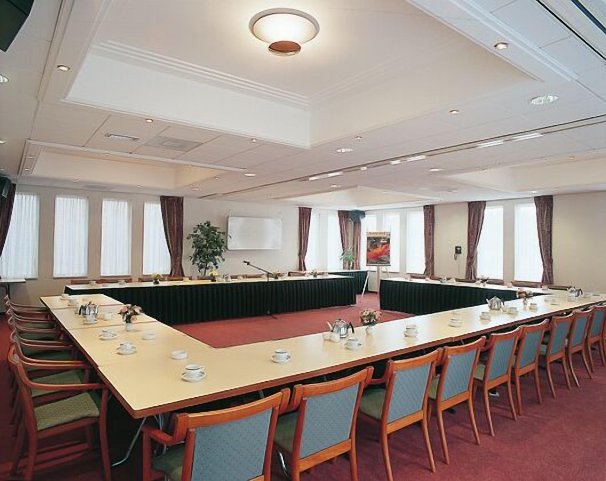 Een congreszaal met een lange tafel, meerdere stoelen en een whiteboard.