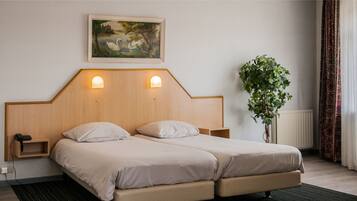 Uma cama de casal com cabeceira de madeira, mesas de cabeceira, um quadro acima da cama e um vaso com planta ao lado da janela.