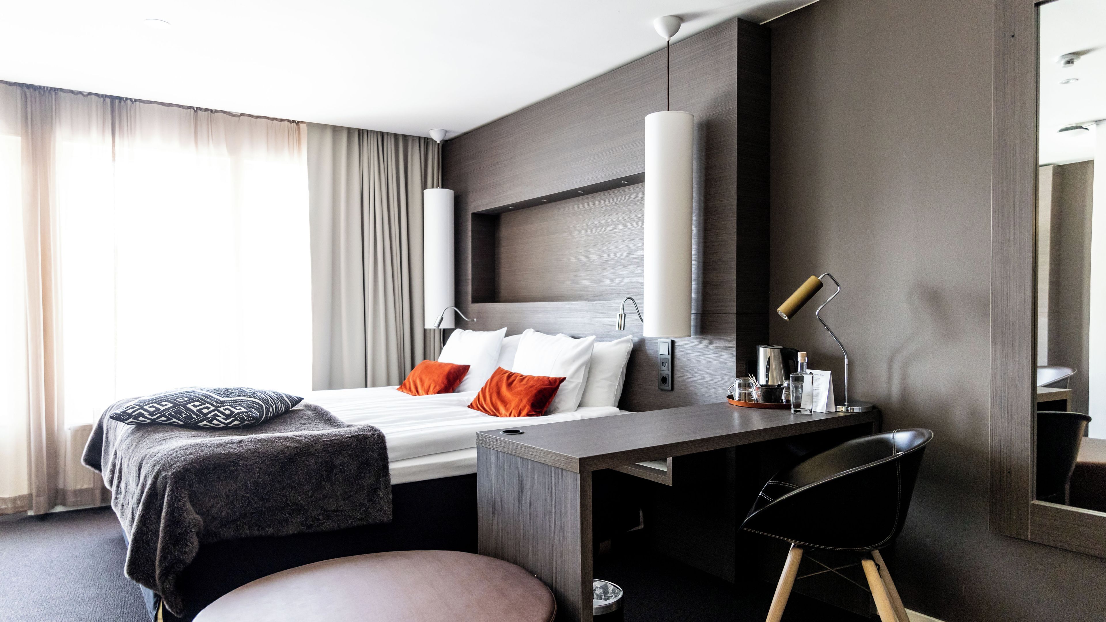 Ein modernes Hotelzimmer mit Bett, Schreibtisch, Stuhl und einem großen Spiegel.