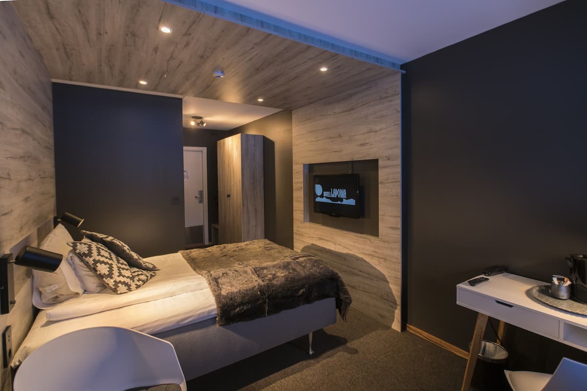 A modern bedroom with a bed, bedside table, and a TV mounted on the wall.