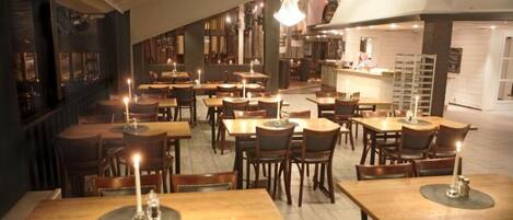 Un restaurante con varias mesas y sillas, velas en cada mesa y una barra de fondo.