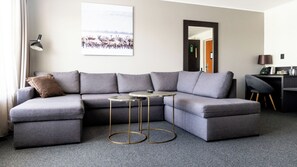 A modern living room with a grey sectional sofa, a small round coffee table, and a desk with a chair. - Hotell Laponia (Arvidsjaur)