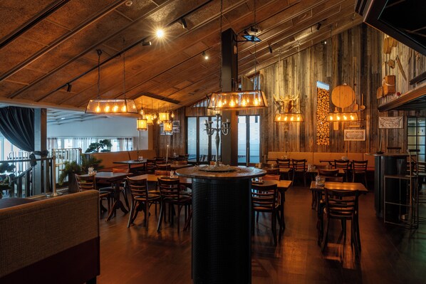 A restaurant interior with wooden walls, hanging light fixtures, and a central fire feature. - Hotell Laponia (Arvidsjaur)