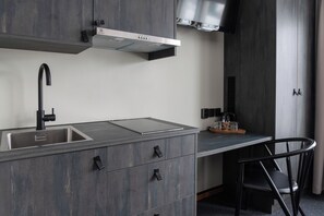 A modern kitchen with a built-in sink, a range hood, and a countertop with a glass-top stove. - Hotell Laponia (Arvidsjaur)