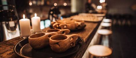 A bar setting with wooden mugs on a tray, candles, and glasses on the counter.