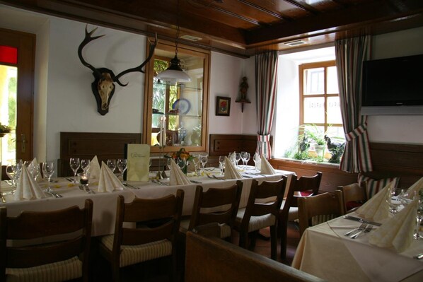 A dining area with wooden tables set for a meal, a mounted deer skull on the wall, and a television above the window.