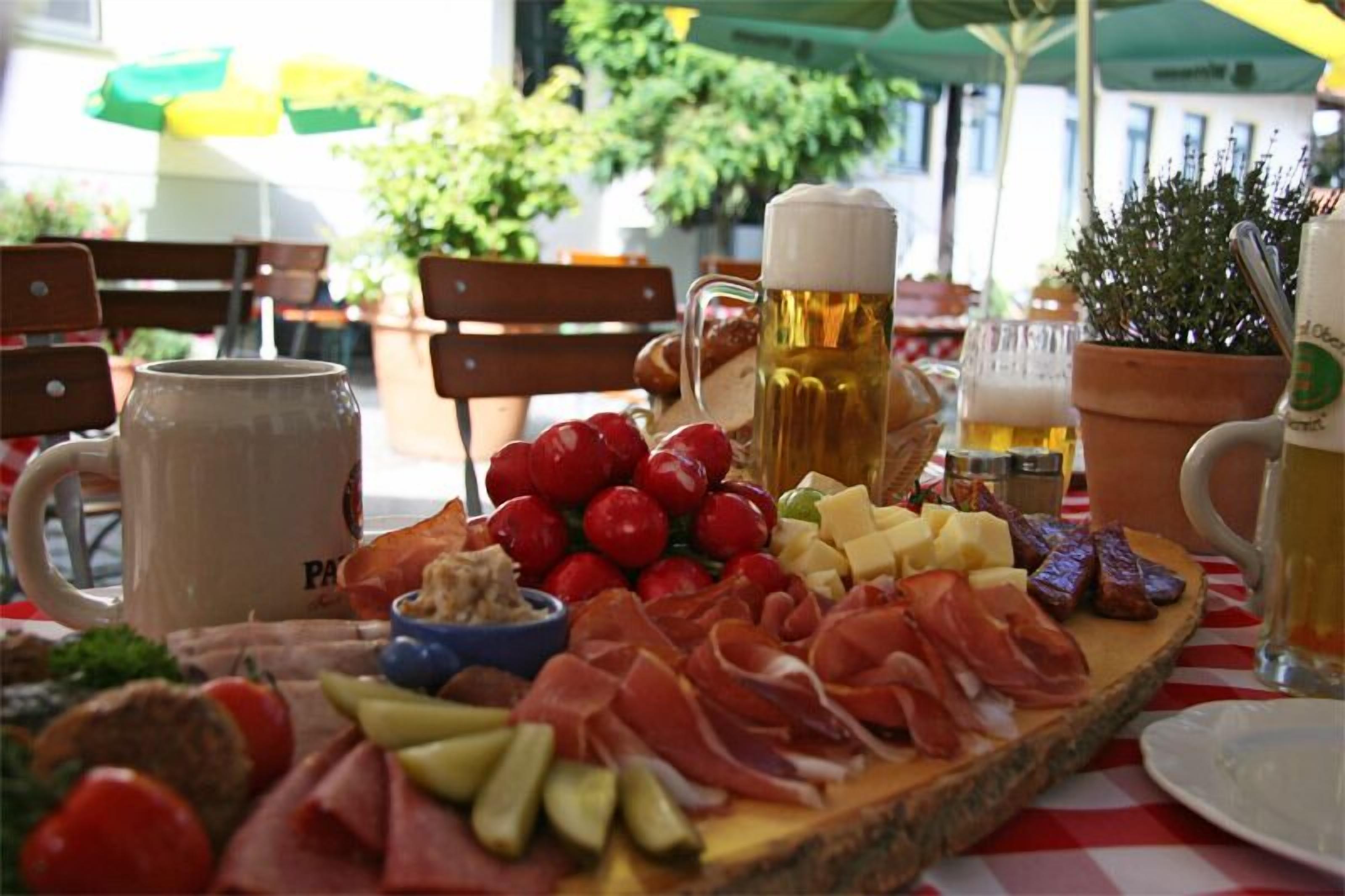 Eine Platte mit verschiedenen Wurstwaren, Käsesorten und Früchten, dazu Bierkrüge und ein Glas Bier.