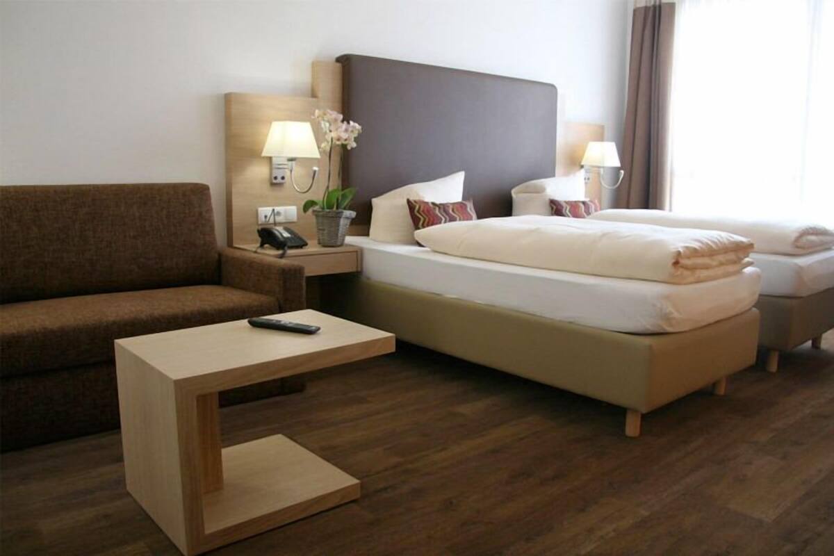 Une chambre d’hôtel avec un lit, un canapé, une petite table et une table de chevet avec une lampe et un téléphone.